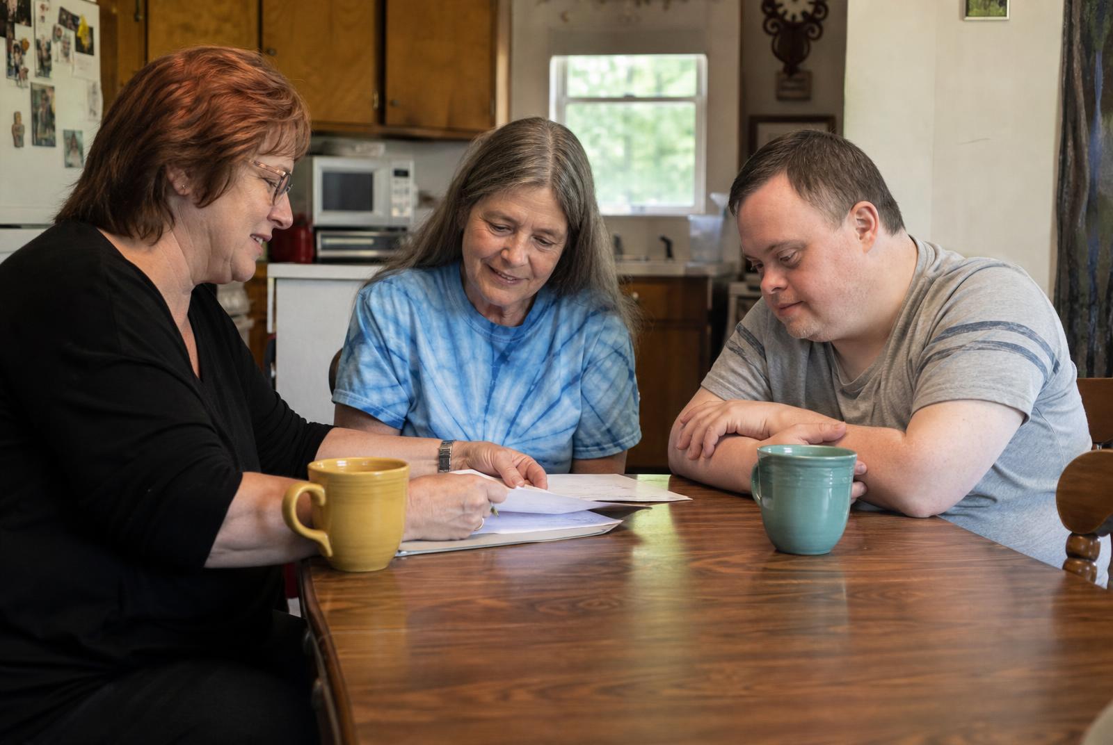 Two men sitting at a sunlit kitchen table reviewing a support plan together