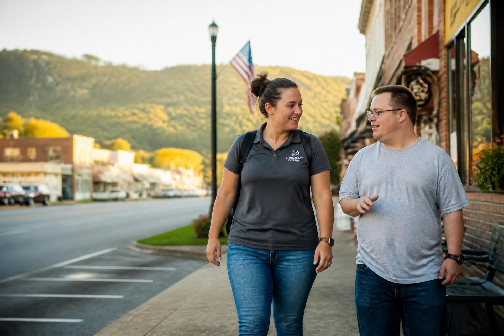 A support worker and a man walking and talking together along a small town street in East Tennessee