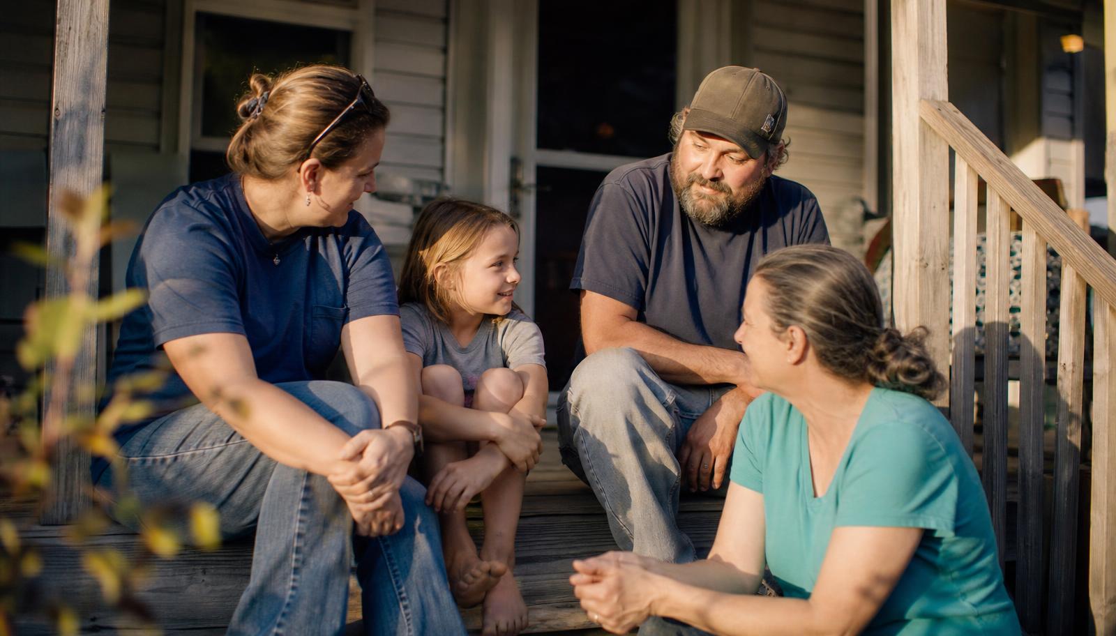 A family and a support worker sitting together on the porch steps of a home in East Tennessee at golden hour
